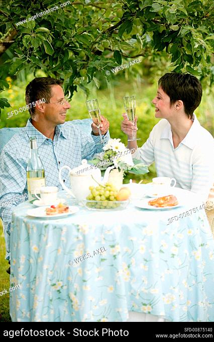 Young couple having champagne breakfast in garden