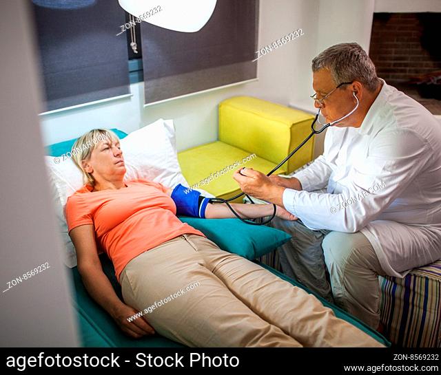 Senior woman is under doctor control at home. Man checking blood pressure using tonometer and stethoscope