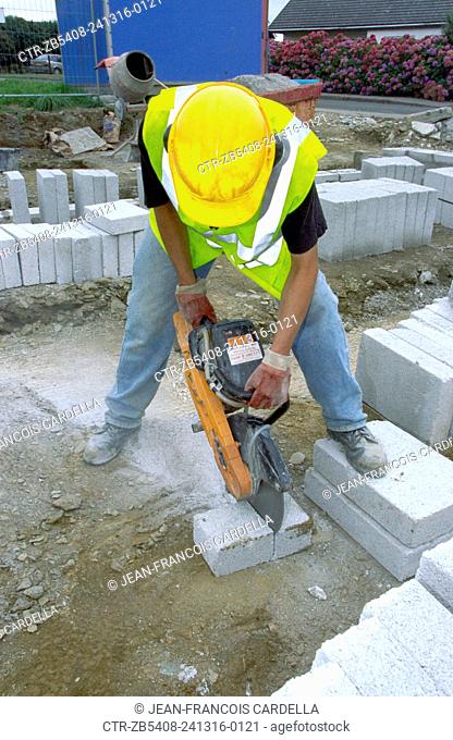 Young builder cutting concrete bricks with a petrol cutter