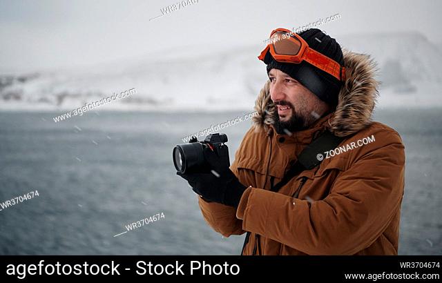photographer tourist explorer at winter in stormy weather wearing warm fur jacket and taking photos photos of nature and landscapes