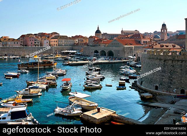 Old town of Dubrovnik and the sea port with many boats and yachts in Croatia. There is a fort, fortification walls, old houses with shingled red-orange roofs