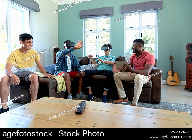 Multiracial male friends looking through virtual reality simulators while sitting on sofa at home