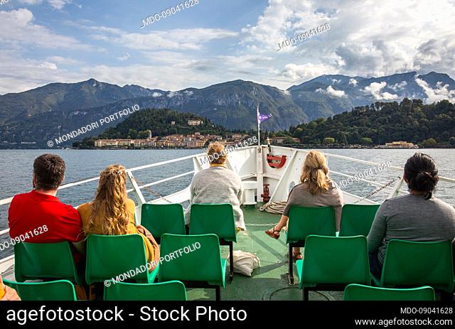 Some tourists from behind and sitting on the bow of a motor ship sailing on Lake Como (Italy), September 29th, 2021