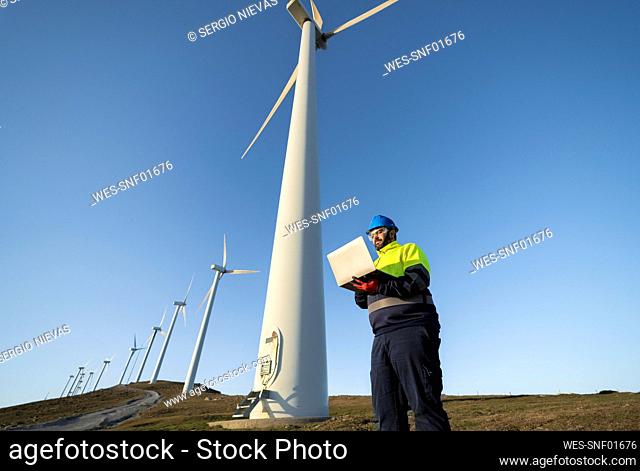 Technical engineer using laptop near tall wind turbines