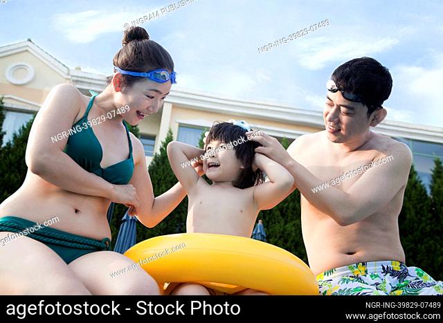 Smiling happy family helping son put on goggles by the poolside