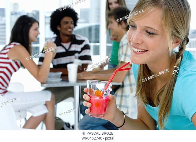 Close-up of a young woman holding a glass of juice in a restaurant with her friends sitting in the background