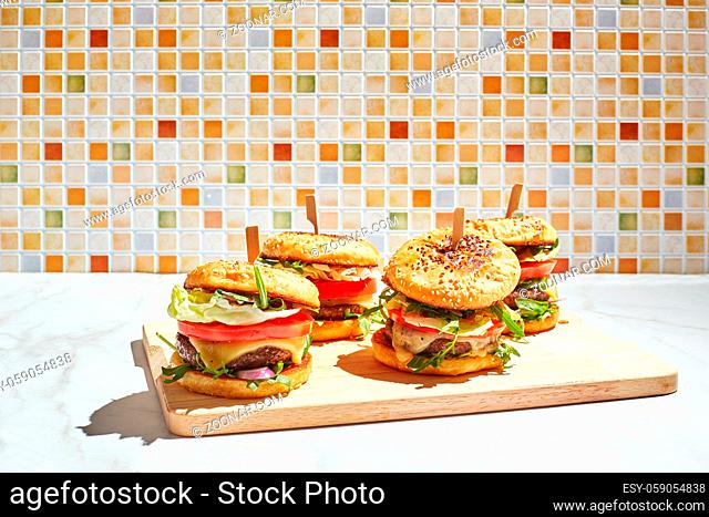 Appetizing homemade burgers on wooden cutting board with bright sunlight. Burger with veal cutlets, pamidorom, cheese, red onion, lettuce