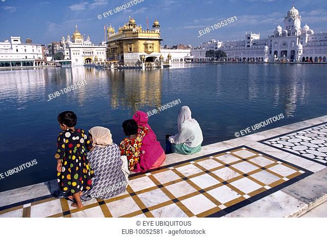 Golden Temple. Sikh women and children sitting at the side of the sacred pool looking towards the temple