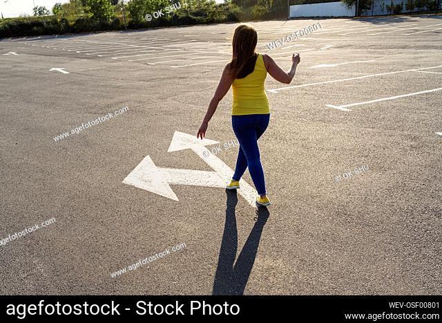 Woman walking on asphalt with arrow symbol