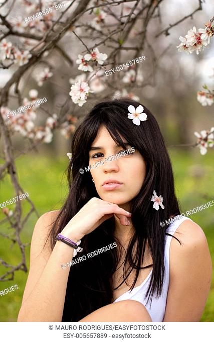 View of a beautiful girl on a white dress on a green grass field next to a almond tree