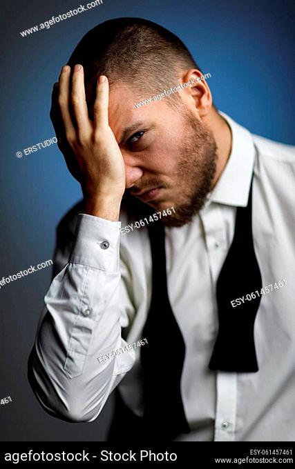 emotional male portrait. upset bearded man in white shirt and untied bow tie on dark blue background