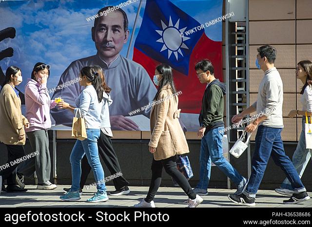Passersby walk by an image of Sun Yat-sen - Chinese politician and revolutionary, leader and founder of the Kuomintang, Considered the founder of modern and...