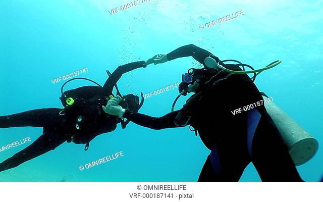 Older male and female scuba divers partner dancing underwater