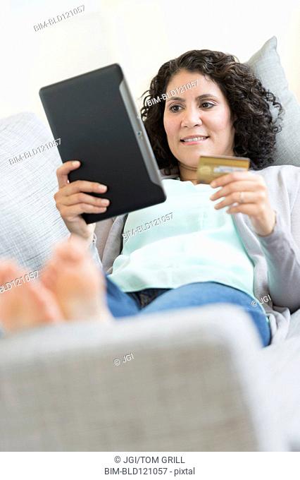 Hispanic woman using digital tablet on sofa