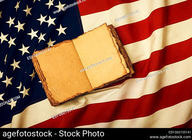 Close up vintage book blank yellow paper pages on old weathered cotton embroidered US national flag background, symbol of American history heritage