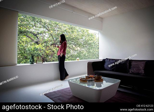 Young woman drinking tea at window in modern living room