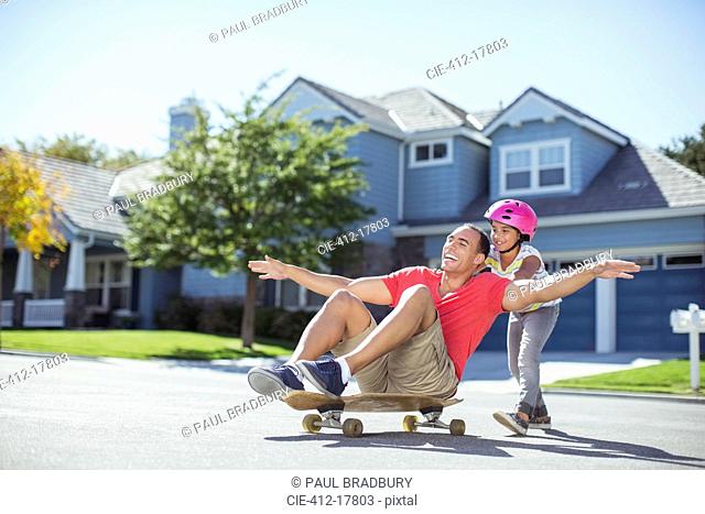 Daughter pushing father on skateboard