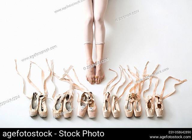 Many pairs of ballet shoes in pairs stand in a row. Legs of a young ballerina with bare feet. The girl's fingers are all covered in wounds and plasters