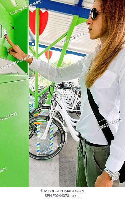 Young woman using machine at electric bicycle sharing station