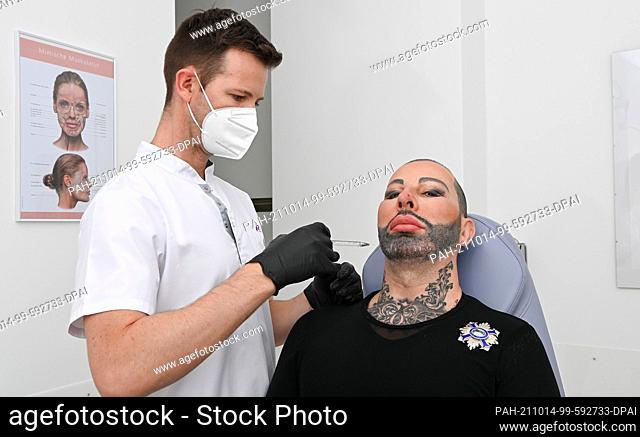 13 October 2021, Berlin: Fashion designer Harald Glööckler (r) has his cheeks injected by Milos Zoric at the Medicalthree plastic surgery clinic on...
