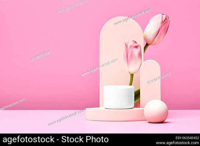 White jar of cosmetic premium product on podium with pink tulips and elegant arch on pastel pink background. mock up