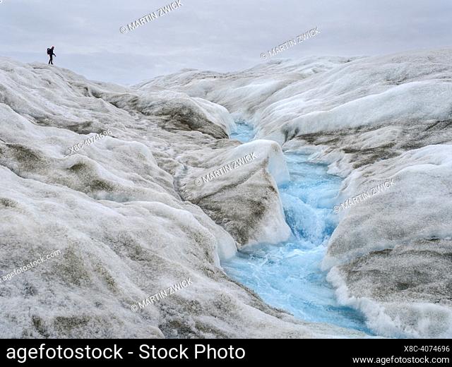 Tourists hiking on the ice. The brown sediment on the ice is created by the rapid melting of the ice. Landscape of the Greenland ice sheet near Kangerlussuaq