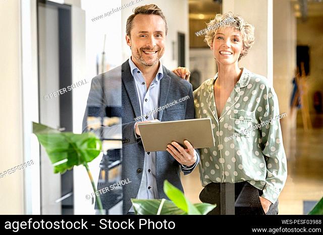 Happy businessman and businesswoman standing with tablet PC in office