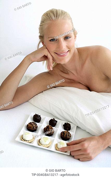 Portrait of young woman lying on bed with tray of pastries