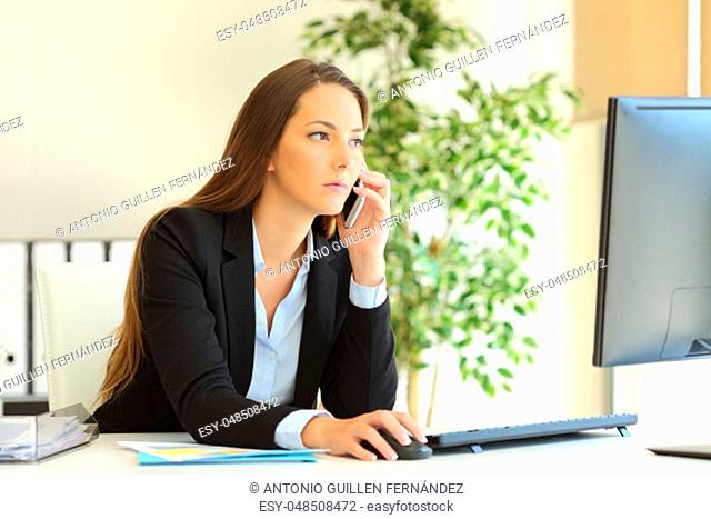 Concentrated businesswoman talking on the phone and checking information in a desktop computer