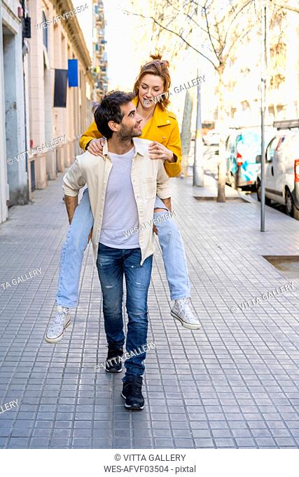Man giving girlfriend a piggyback ride on pavement in the city