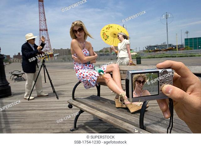 Young woman sitting on a bench with a senior man photographing a senior woman in the background, Parachute Drop, Coney Island, New York City, New York, USA