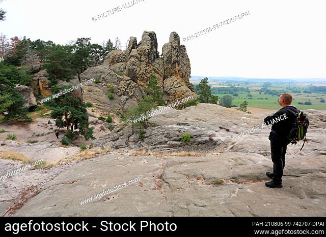 05 August 2021, Saxony-Anhalt, Timmenrode: A hiker walks along the path leading over the Devil's Wall to Blankenburg to the rock formation ""Drei Zinnen""