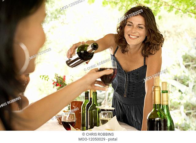 Two women at dinner party one pouring wine for other