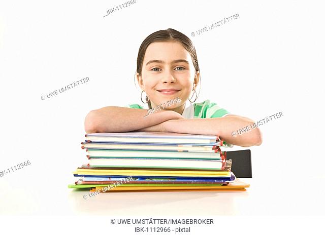 Smiling girl sitting in front of a pile of exercise books and school books