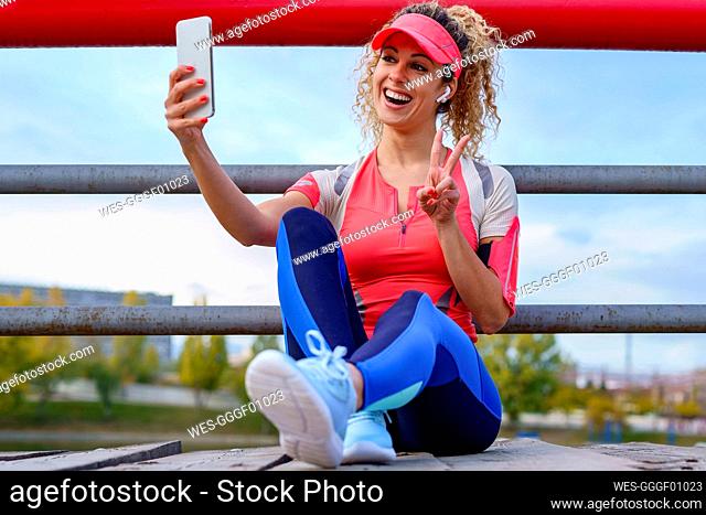 Happy sportswoman taking selfie sitting on footbridge