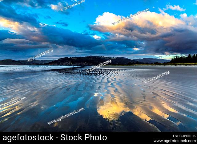 Low tide. Strips of sand and water left by the ocean tide. Sunrise over the ocean. New Zealand, Pacific Coast. The concept of artistic photography