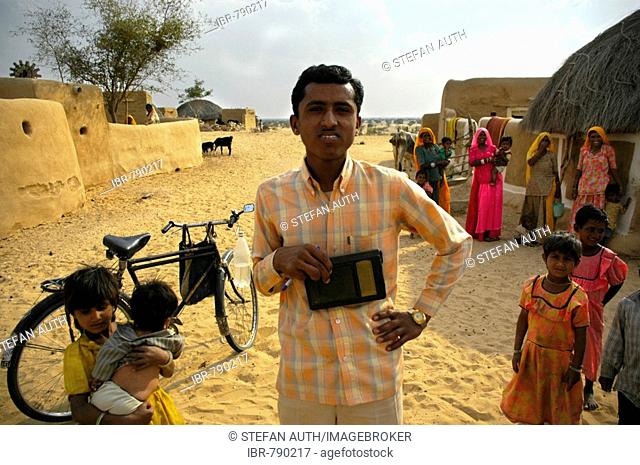 Young Indian man holding a radio standing in front of a bicycle among other people in a village in the Thar Desert near Jaisalmer, Rajasthan, India