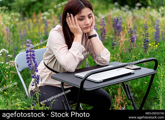 Tired freelancer at desk sitting in lupine flowers meadow