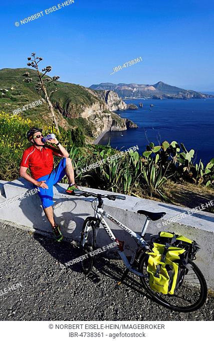 Cyclist pausing on the Belvedere Quattrocchi with a view over the rocks Faraglione on the island Vulcano, Pianoconti, Lipari, Aeolian Islands, Sicily, Italy