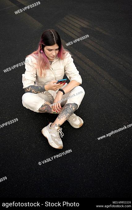 Fashionable young woman with tattoo using smart phone in spots court