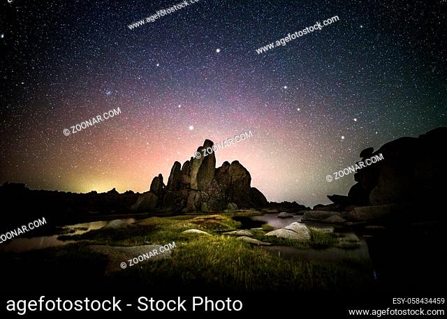 Starry night sky over Snowy Mountains Australia. Large rocky tor surounded by icy waters, tufted grasses and little flowers