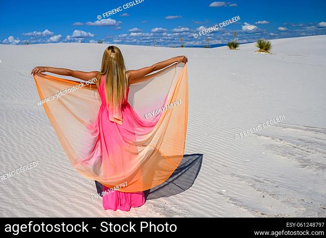 Dream-like scene. Elegant woman, wearing a fancy dress and standing like a fairy among the Yuccas at sunset in the desert of White Sands National Monument