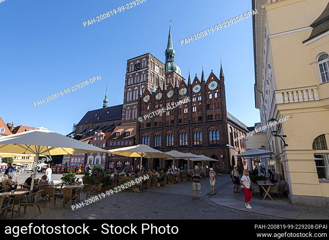 13 August 2020, Mecklenburg-Western Pomerania, Stralsund: Holidaymakers sit in a restaurant on the Old Market Square, behind which stands the Gothic town hall...