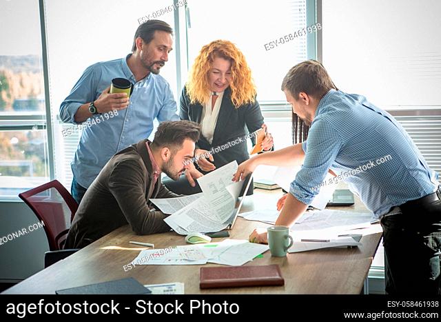 Business people looking through documents all together and happy smiling while working in team in board room in office interior. Teamwork concept