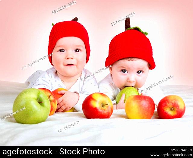 two cute six month old babies lying in hats on soft blanket with apples