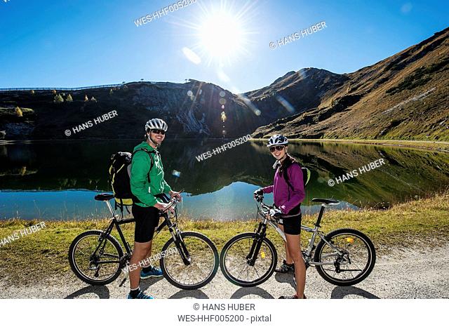 Austria, Altenmarkt-Zauchensee, young couple with mountain bikes at mountain lake