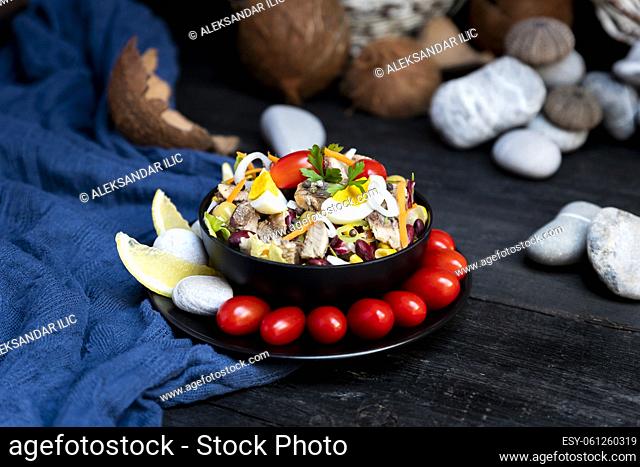 Fish salad with sardines, harringe, tuna, tomato, lemon, lettuce, cabbage, olives, beans, corn, carrotes and eggs on rustic kitchen table