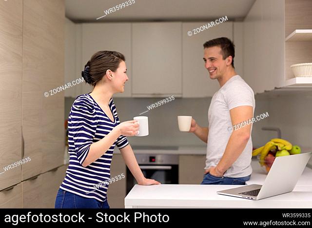 happy young couple with laptop computer enjoying morning coffee in modern kitchen at home