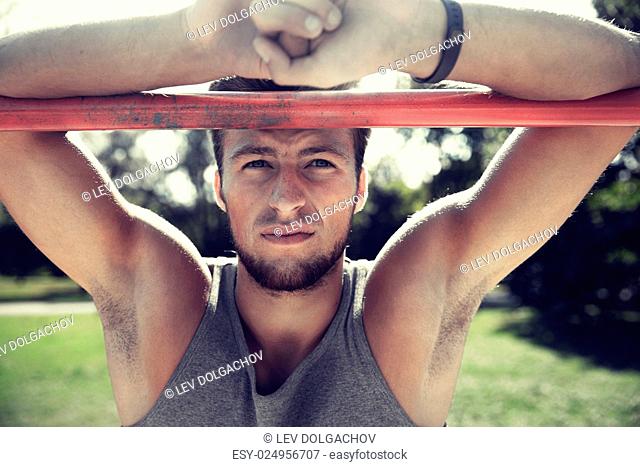 fitness, sport, training and lifestyle concept - young man with heart-rate watch bracelet exercising on horizontal bar in summer park