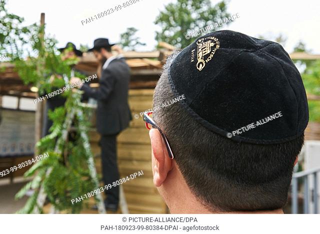 23 September 2018, Berlin: A Jewish parishioner watches the rabbis Yehuda Teichtal and Shmuel Segal (l-r) decorate a leaf hut. On 23.09